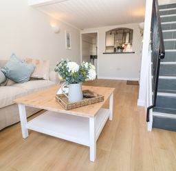 A living room with a beige sofa and blue cushions a wooden coffee table with a flower vase and a staircase with dark tiles at 58 High Street Falmouth