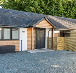 An entrance of a single story house with wooden paneling a black door and gravel driveway at Clonmore in Bodmin