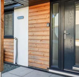 A front door with glass panels beside wooden paneling and a white wall with a water tap at Clonmore in Bodmin