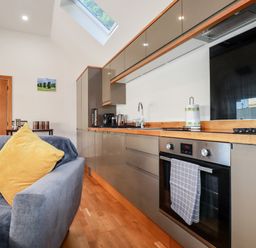 A kitchen with grey cabinets wooden countertops an oven a sink and a gray couch with a yellow pillow at Clonmore in Bodmin