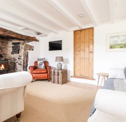 A living room with a stone fireplace wood stove a brown leather armchair a white sofa and a wooden door at Trelash Cottage Trelash near Boscastle