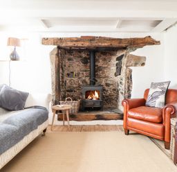 A living room with a wood stove fireplace a leather armchair a sofa with cushions and a lamp at Trelash Cottage Trelash near Boscastle