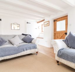 A living room with two sofas and cushions a wooden door and white walls at Trelash Cottage in Trelash near Boscastle