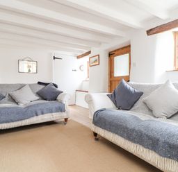 A sitting room with two sofas, cushions, wooden door, and small staircase at Trelash Cottage in Trelash near Boscastle