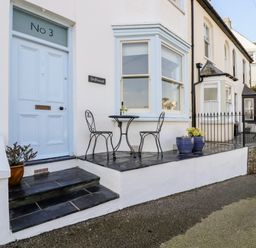 A front porch with a blue door and a small table with two chairs outside Driftwood in Fowey