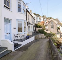 A row of houses along a narrow curved street with outdoor seating areas at Driftwood in Fowey
