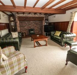 A living room with green leather sofas a plaid armchair a wooden coffee table a brick fireplace and exposed wooden beams at The Granary in Longhirst near Morpeth