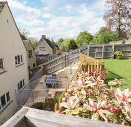 A garden with a lawn, plants, a patio area with a table and chairs, and a fenced house at White Stones in Fulbrook near Burford