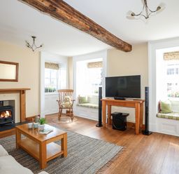 A living room with a wooden beam ceiling a fireplace a rocking chair and two window seats at Above Deck in Beaumaris