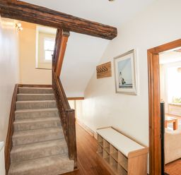 A staircase with carpet and wooden banister next to a wooden framed doorway leading to a living room with a window seat at Above Deck in Beaumaris