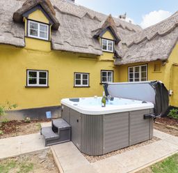 A courtyard with a hot tub and steps outside a yellow thatched cottage at The Abbey Cottage in Windsor Green
