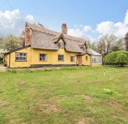 A yellow thatched cottage with a conservatory and lawn with croquet equipment at The Abbey Cottage in Windsor Green