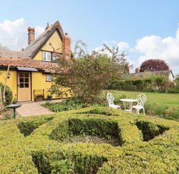 A garden with a trimmed hedge and white metal table and chairs outside a yellow cottage at The Abbey Cottage in Windsor Green
