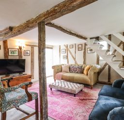 A living room with a beige sofa blue armchair patterned chair and pink rug at The Abbey Cottage in Windsor Green