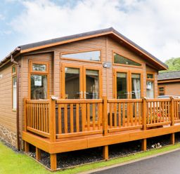 A wooden lodge with a deck and railings on a grassy area at Hafan Lodge 85 Wisemans Bridge near Saundersfoot