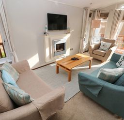 A living room with beige and blue sofas a wooden coffee table a wall-mounted TV and a fireplace at Hafan Lodge 85 Wisemans Bridge near Saundersfoot