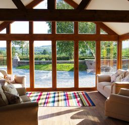 A room with large wooden framed windows beige sofas and a colorful striped rug at Haimwood Byetake in Llandrinio