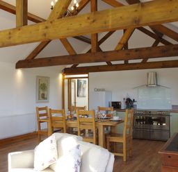 A kitchen and dining area with wooden beams a table with chairs and kitchen appliances at Haimwood Byetake Llandrinio