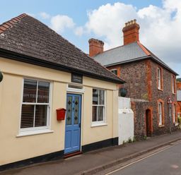 A street view of a cream coloured cottage with a blue door and red mailbox at Hardings cottage in Minehead
