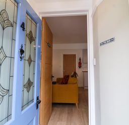 View through an open blue door with stained glass into a hallway with a yellow sofa and wooden doors at Hardings cottage in Minehead