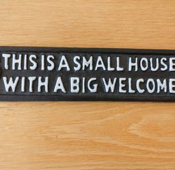 A black sign with white text saying this is a small house with a big welcome on a wooden surface at Hardings cottage in Minehead