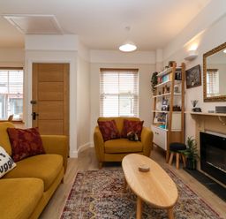A living room with yellow sofas a wooden coffee table a fireplace a mirror and a bookshelf at Hardings cottage in Minehead