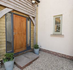 An exterior wooden door with glass side panels between two potted plants and a small window on a white wall at Little Knaplock in Fiddington near Combwich Somerset