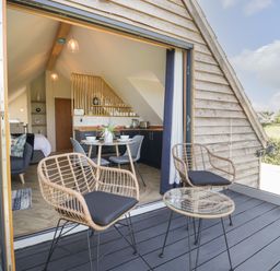 A balcony with two chairs and a table overlooking a field with an open door leading to a kitchen and dining area at Little Knaplock in Fiddington near Combwich Somerset