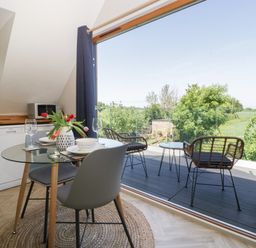 A dining area with a glass table set for two next to an open door leading to a balcony with two chairs and a table at Little Knaplock in Fiddington near Combwich Somerset