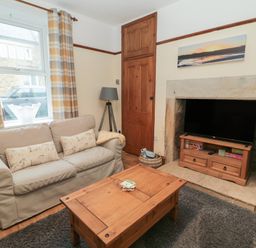 A living room with a beige sofa wooden coffee table and television on a stand in a stone fireplace at Coras House in Amble