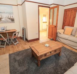 A living room with a wooden coffee table a gray rug a small dining table with chairs and a sofa with cushions at Coras House in Amble