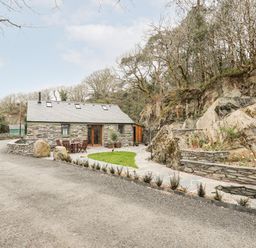 A stone cottage with outdoor table and chairs next to a rock face and garden at Tyn Llwyn Cornel Eco Barn in Garreg