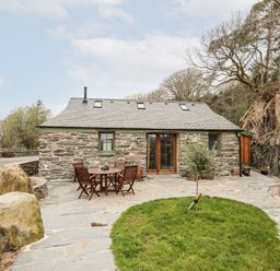 Stone cottage with a patio table and chairs and a small tree on a stone patio at Tyn Llwyn Cornel Eco Barn in Garreg