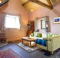 A living room with a wood stove a sectional sofa and a wooden coffee table at Tyn Llwyn Cornel Eco Barn in Garreg