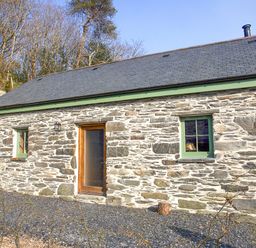 Exterior view of a stone cottage with two windows and a door in a wooded area at Tyn Llwyn Cornel Eco Barn in Garreg