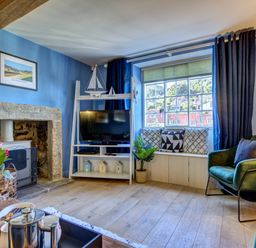 A living room with a stone fireplace a television on a white stand and a window seat with cushions at Crab Cottage in Sandsend