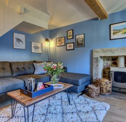 A living room with a blue sofa coffee table flowers fireplace and framed pictures on blue walls at Crab Cottage in Sandsend