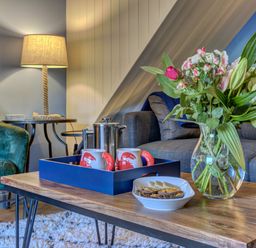 A living room with a wooden coffee table holding a vase of flowers mugs a teapot and a bowl of snacks at Crab Cottage Sandsend