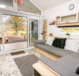 A living room with a gray sofa and patterned pillows near sliding glass doors with a view of a tree at Oak Tree View in Nantmel near Rhayader