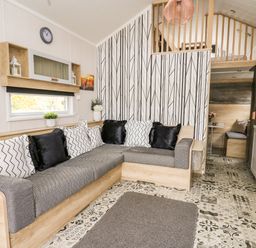 A living room with a gray and wood sofa with black and white pillows a patterned rug and a small kitchen at Oak Tree View in Nantmel near Rhayader