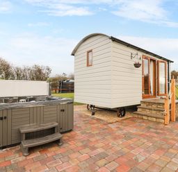An outdoor area with a hot tub and a small building with wooden steps and chairs at Highland View in Rhayader