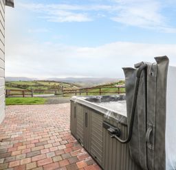 An outdoor hot tub on a brick patio next to a building with a view of rolling hills and fields at Highland View in Rhayader