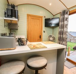A small kitchen area with a countertop, two stools, a toaster, a knife block, a wall-mounted TV, and a door leading outside at Highland View in Rhayader