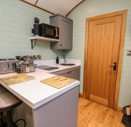 A small kitchen with a wooden door a countertop with two stools microwave toaster and a fan at Highland View in Rhayader
