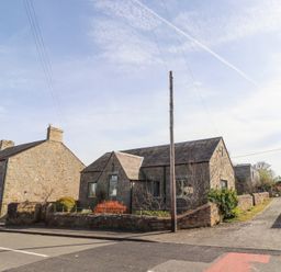 A street view of stone houses with fenced gardens and a utility pole at The Old School in Lowick