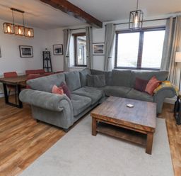 A living room with a gray sectional sofa wooden coffee table dining table with chairs and framed pictures on the wall at The Old School in Lowick