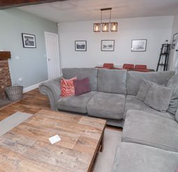 A living room with a grey sectional sofa and wooden coffee table near a fireplace and dining area at The Old School in Lowick