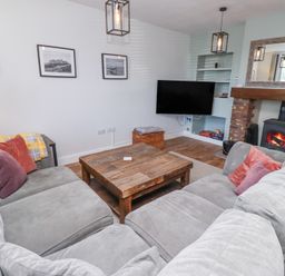 A living room with grey sofas and a wooden coffee table a fireplace with a fire and a wall-mounted television at The Old School in Lowick