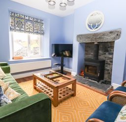A living room with a green sofa and blue chairs around a wooden coffee table near a fireplace at Estcote Roger Ground near Hawkshead