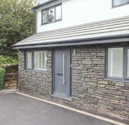 The exterior front of a stone house with a grey door and windows with white blinds